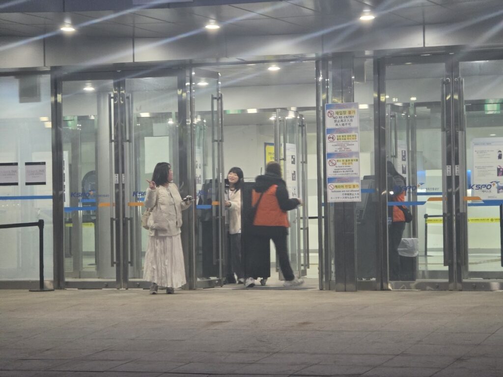 nct-dream-seoul-concert-2026-security-fences A photograph focusing on the gray plastic safety barriers and metal fences set up in front of the arena. Thousands of fans are captured in the background, moving toward the NCT DREAM Seoul Concert 2026 entrance, highlighting the intense scale of crowd control.