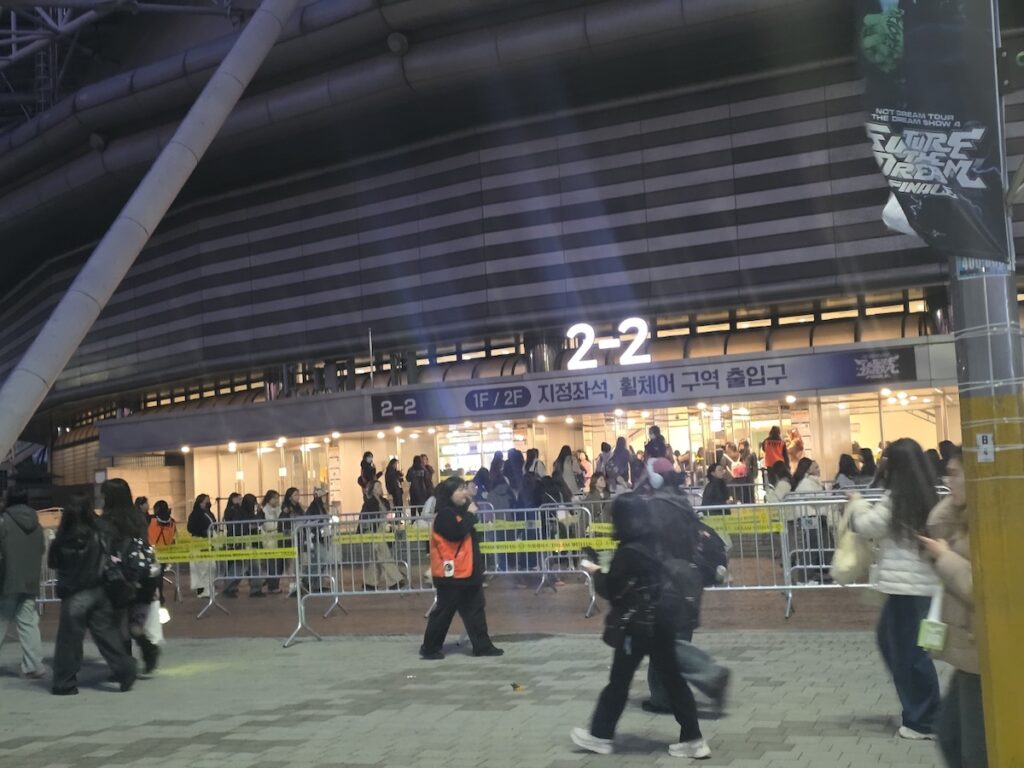 nct-dream-seoul-concert-2026-ticket-check A documentary-style shot of the ticket verification area. Staff members in dark uniforms are visible near the barricades, managing the flow of fans entering the inner circle of the NCT DREAM Seoul Concert 2026 finale.