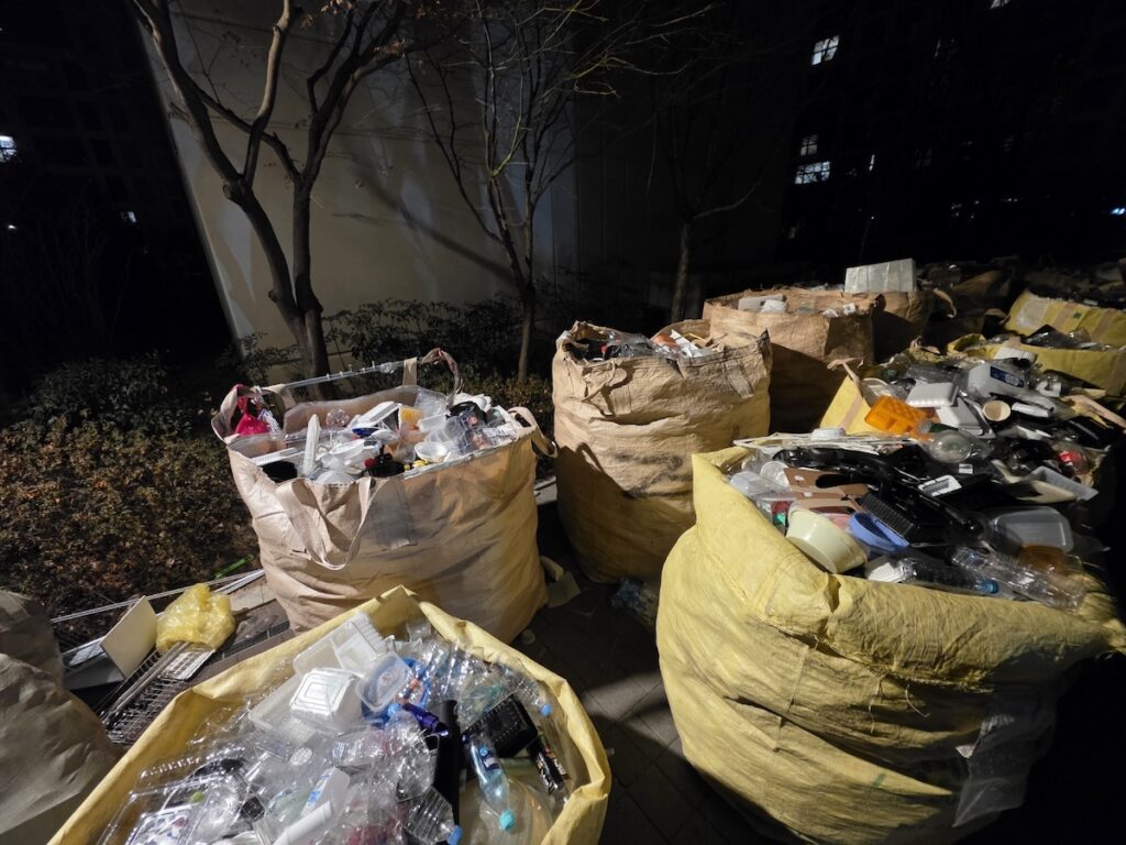 nighttime-recycling-ritual-south-korea-apartments A wide shot of the nighttime recycling ritual in a South Korean apartment block, showing the scale of the community's collective sorting effort.