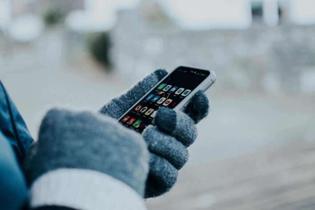 A person using a smartphone with winter gloves, highlighting the seamless connectivity of **Cheap SIM Cards in Korea 2026** during travel.