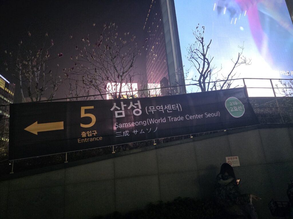 samseong-station-exit-5-world-trade-center-seoul The illuminated nighttime entrance of Samseong Station Exit 5, clearly displaying signs in English and Korean for the World Trade Center Seoul, next to a large media screen in Gangnam.