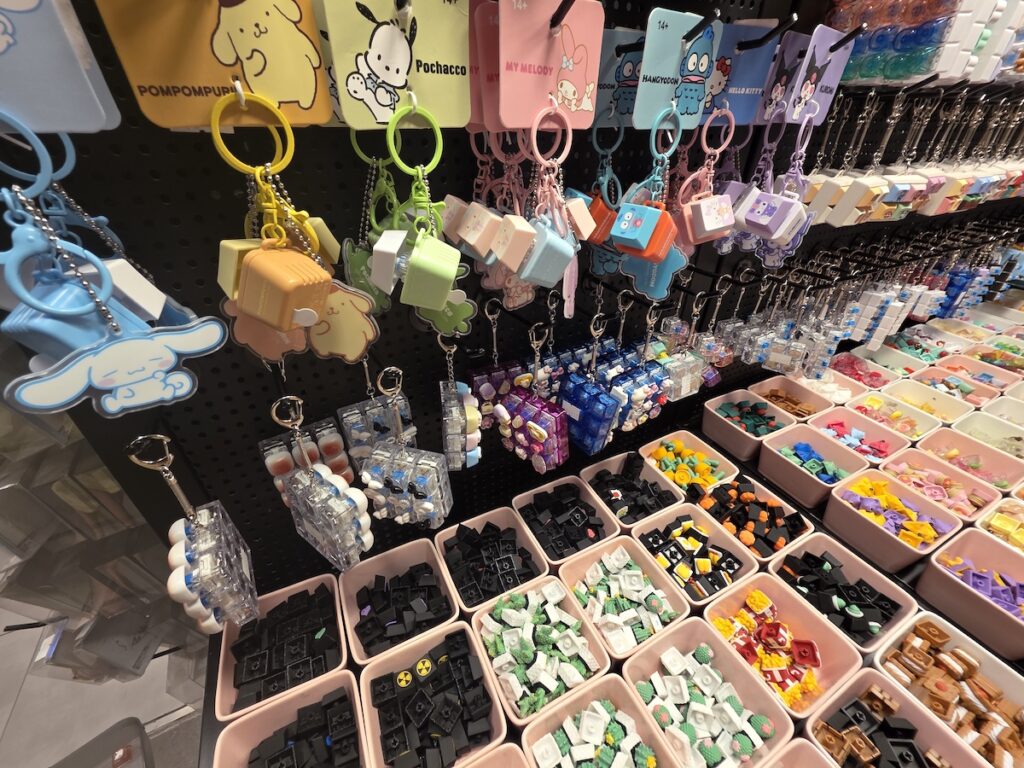 sanrio-korean-keycap-keyring-display A black mesh wall displaying fully assembled Sanrio character mechanical switch keyrings including Hello Kitty and Kuromi designs.