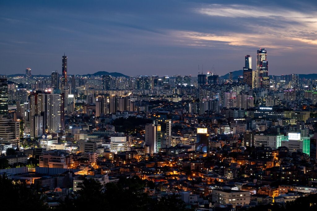 Panoramic view of Seoul city at night, featuring brightly lit skyscrapers, Namsan Tower, and urban lights, used as background for a travel guide.