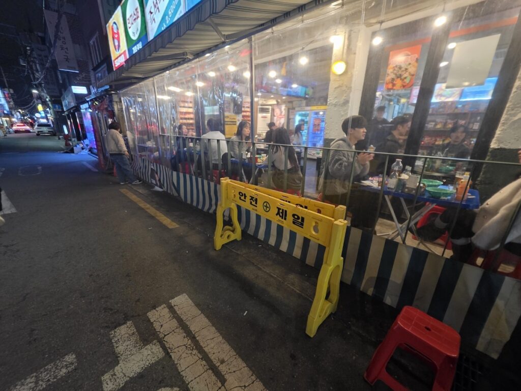 seoul-east-guide-2026-safety-first-night-security A yellow safety barrier in a bright neon alley, proving the high security standards in Seoul East Guide 2026.