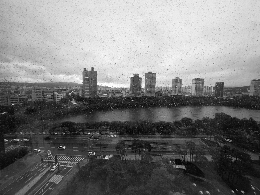A cinematic black and white view of luxury apartments reflecting the Seoul Elite Lifestyle on a rainy day.