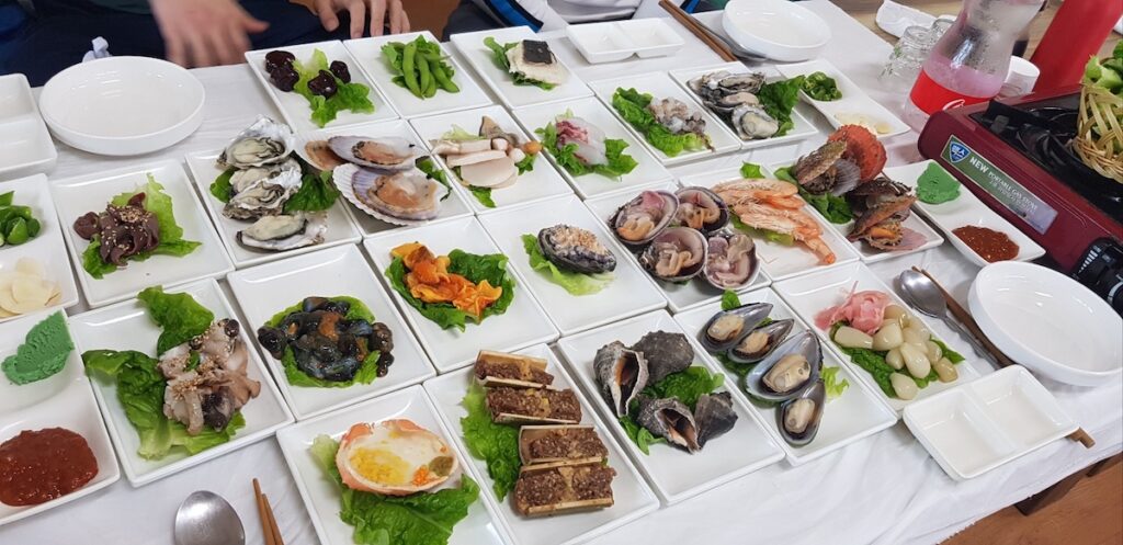 seoul-gastronomic-intelligence-banchan-refill-ritual Complete 2026 guide on how to survive in Seoul as a foreigner showcasing Gastronomic Intelligence with an elaborate array of banchan, including oysters, sea snails, and scallops, highlighting shared dining rituals.