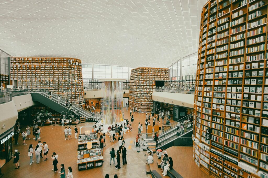 A wide-angle view of a large Korean bookstore aisle, showing towering bookshelves and many customers browsing.