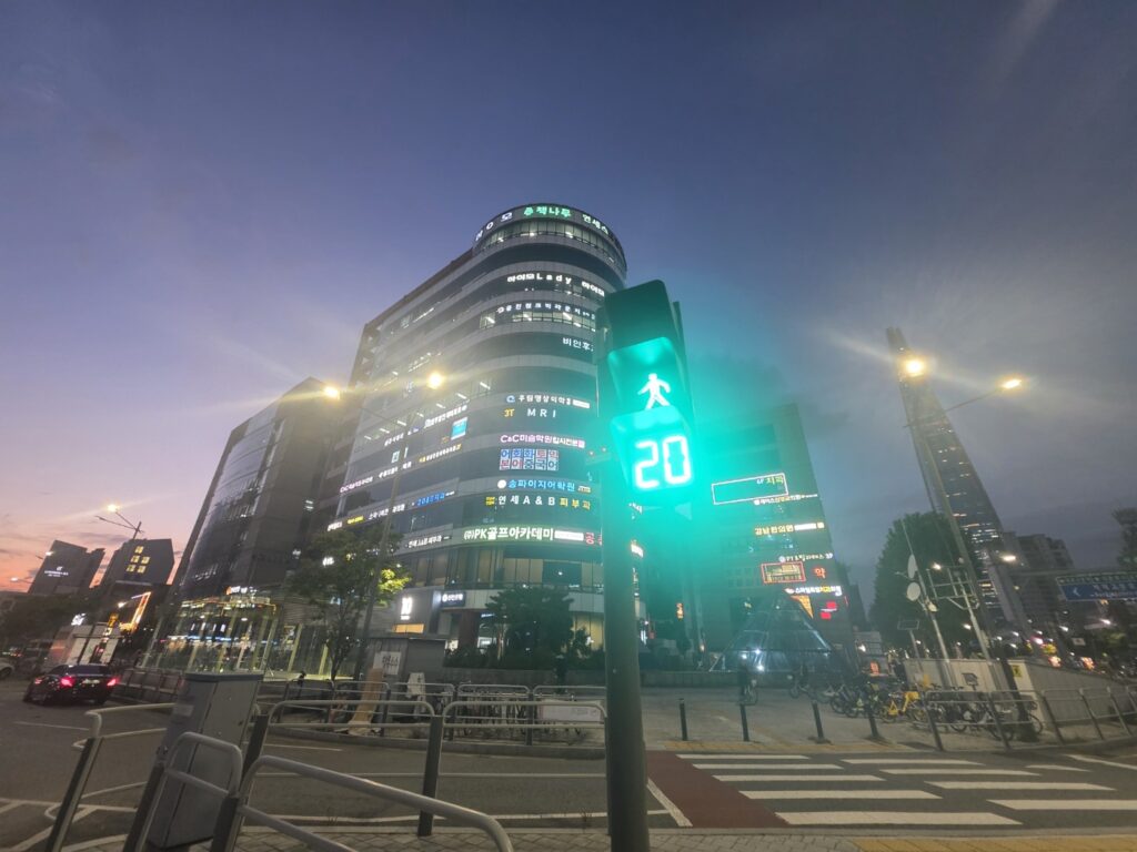 A modern crosswalk in Seoul at dusk with LED countdown lights and tall glass buildings in the background.