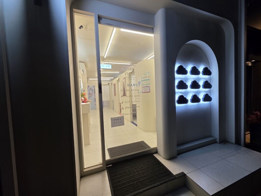 Korean photo booth storefront at night with bright neon signs in a busy Seoul street.