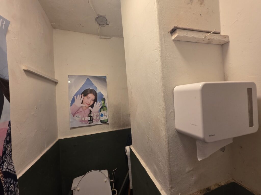 seoul-restroom-rituals-2026-fandom-sanctuary-wall Multiple K-pop posters covering a restroom wall to create a familiar sanctuary as part of Seoul Restroom Rituals 2026.