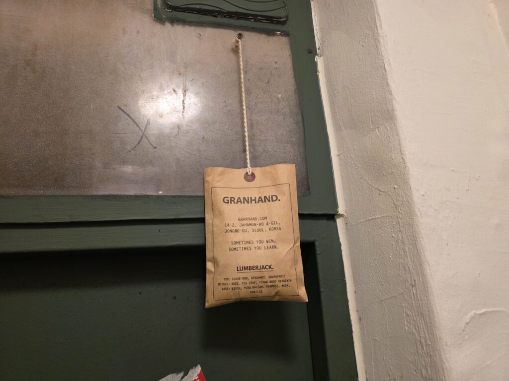 seoul-restroom-rituals-2026-granhand-sachet-ritual A Granhand fragrance sachet hanging on a rusted iron door latch, the ultimate sensory symbol of Seoul Restroom Rituals 2026.