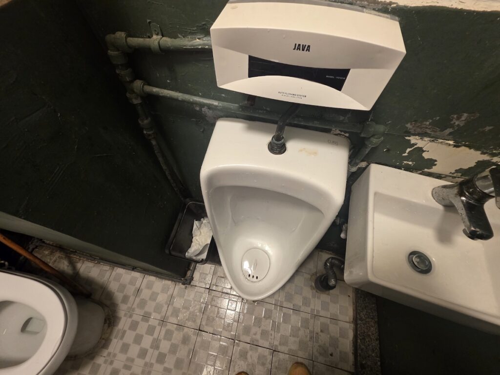 seoul-restroom-rituals-2026-java-hygiene-system A JAVA automatic hygiene sensor installed in an industrial-style restroom, showing the tech-meets-grit side of Seoul Restroom Rituals 2026.