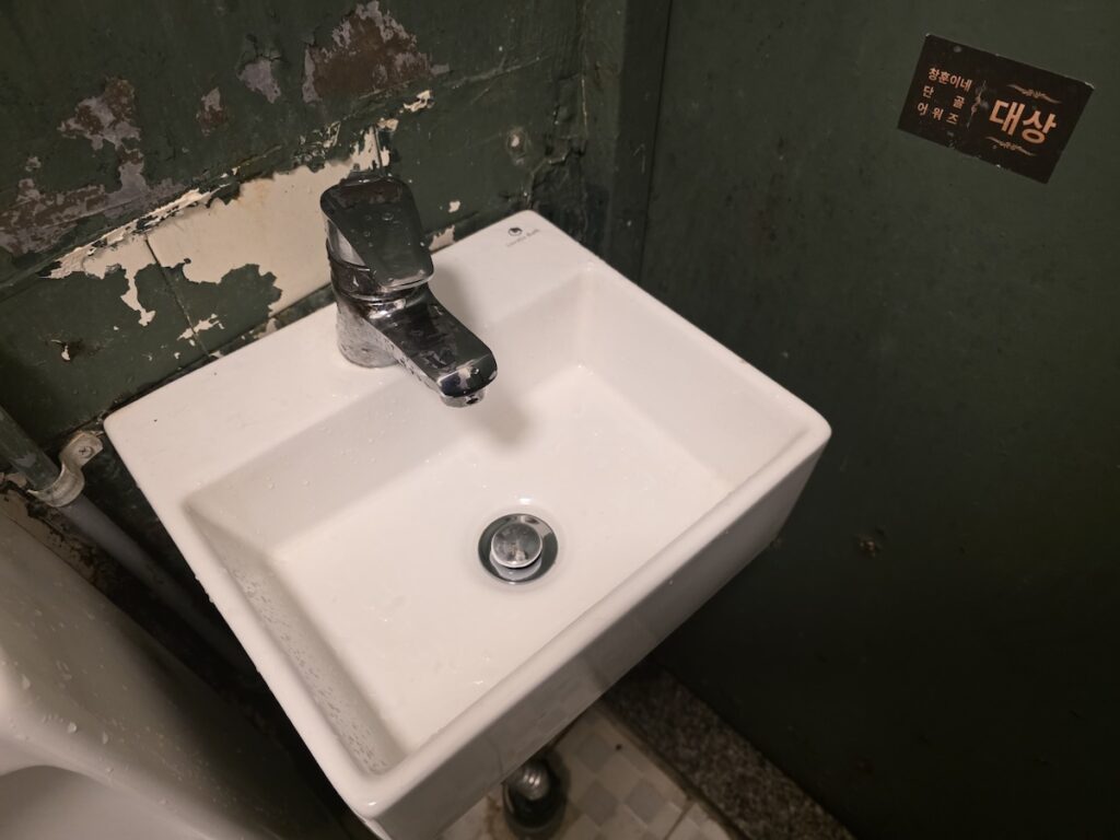 seoul-restroom-rituals-2026-manual-iron-lock-security A sturdy manual iron bolt on a wooden restroom door, representing the private and raw space of Seoul Restroom Rituals 2026.