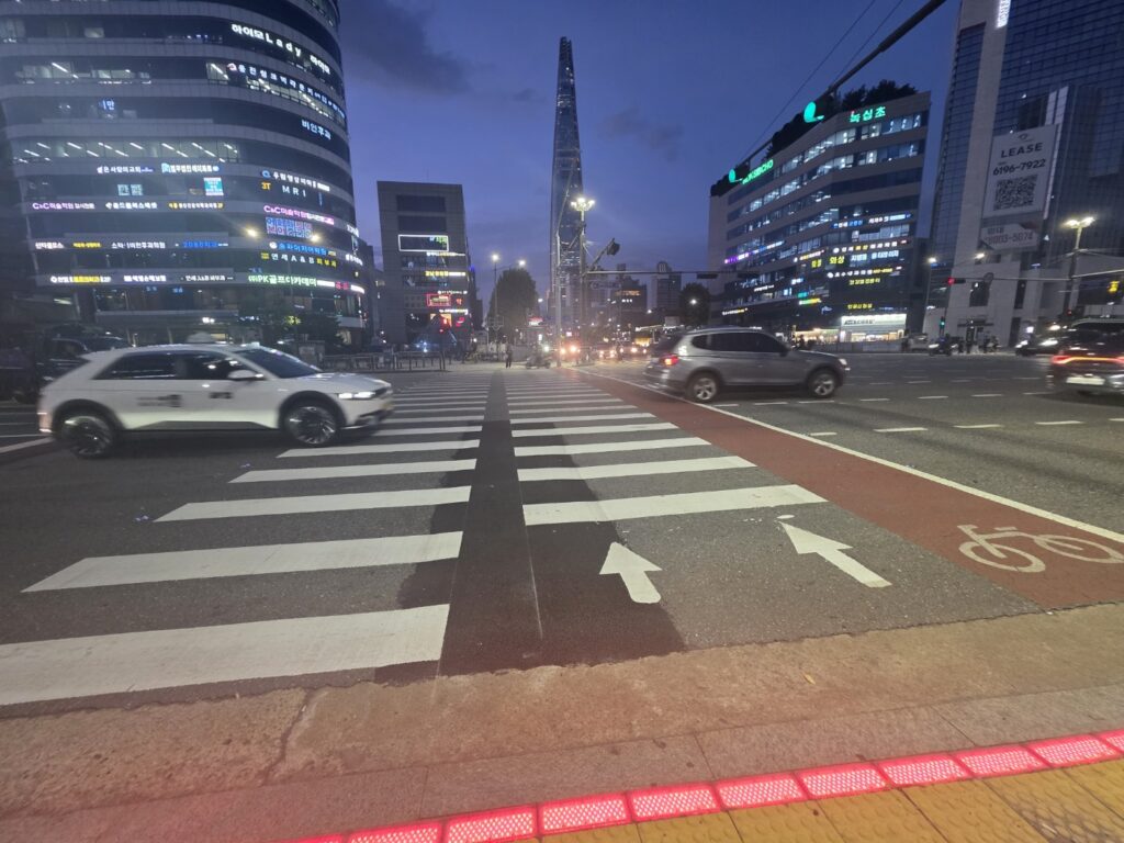 A crosswalk leading toward high-rise buildings in Seoul illuminated by streetlights.