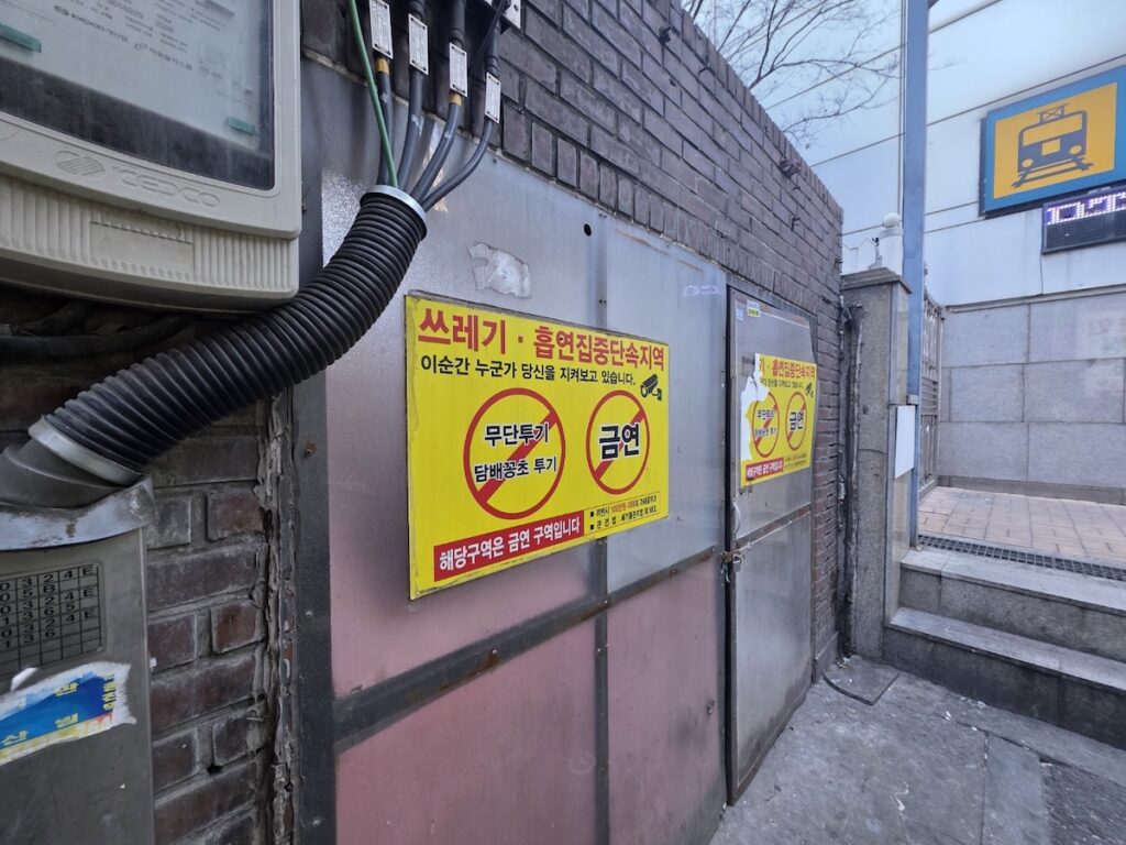 A bright yellow signage illustrating the Seoul Smoking Laws, warning of a 100,000 KRW fine and active CCTV surveillance in a high-enforcement zone.