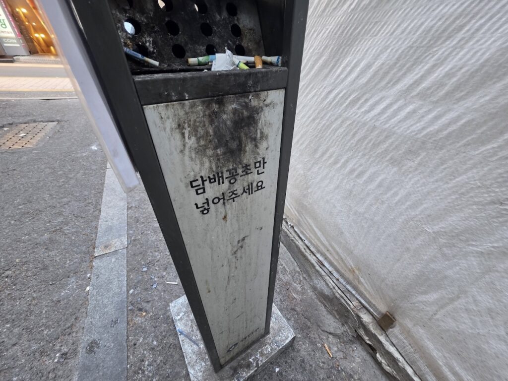 seoul-smoking-laws-designated-ashtray A public ashtray in an alley with a sign in Korean, part of the Seoul Smoking Laws infrastructure designed to manage waste in high-traffic districts.