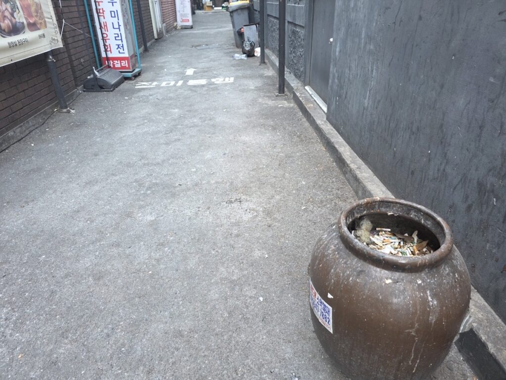 seoul-smoking-laws-local-ashtray-spot A large traditional jar used as an ashtray in a Seoul alley, showing how to identify socially accepted spots under the Seoul Smoking Laws by observing local habits.