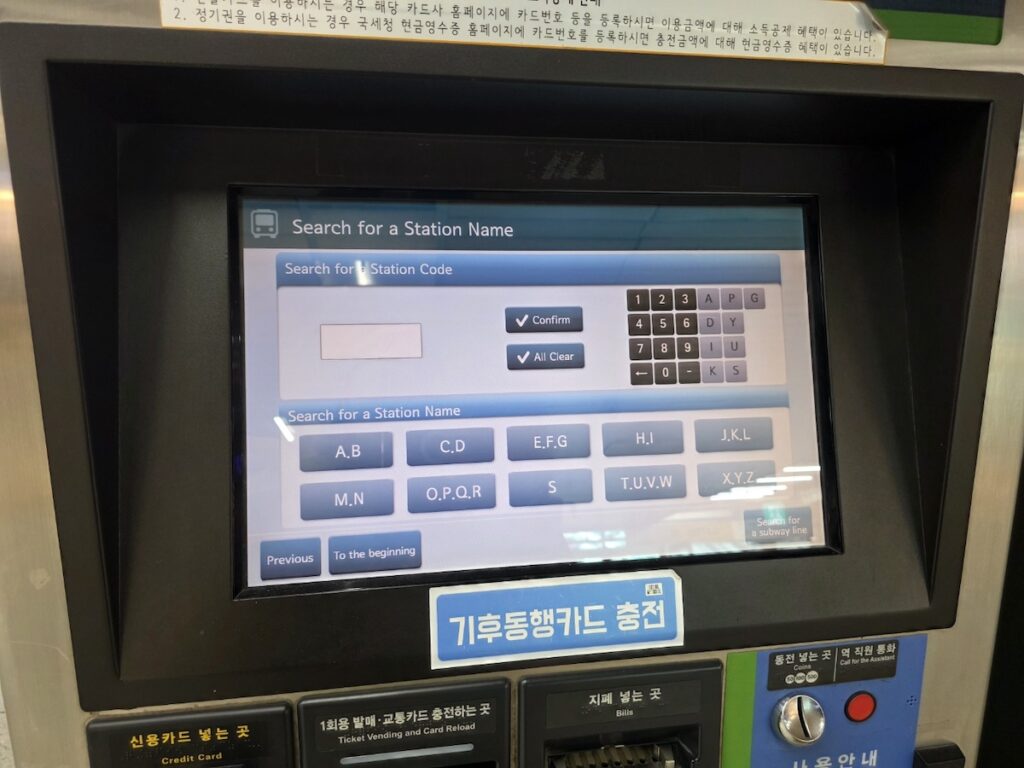 seoul-subway-kiosk-guide-ai-selection-view A strategic Seoul Subway Kiosk Guide visual showing a close-up of the digital interface as a finger selects the English language option on a modern silver ticketing machine.