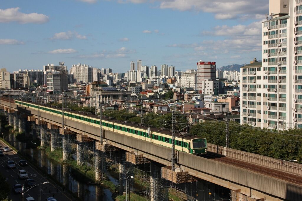 A green Seoul Subway Line 2 train running outdoors on elevated tracks with city buildings and blue sky in the background.