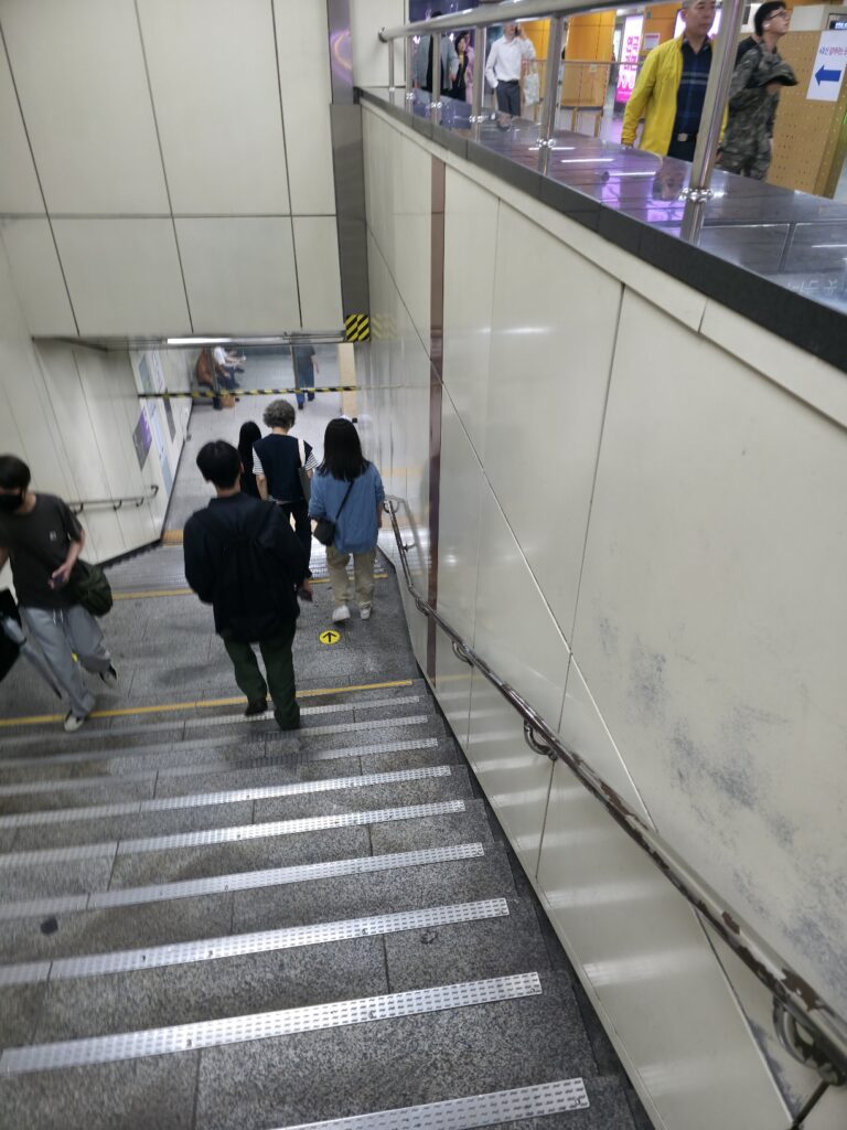 Staircase leading down to a Seoul subway platform with line-color signage.
