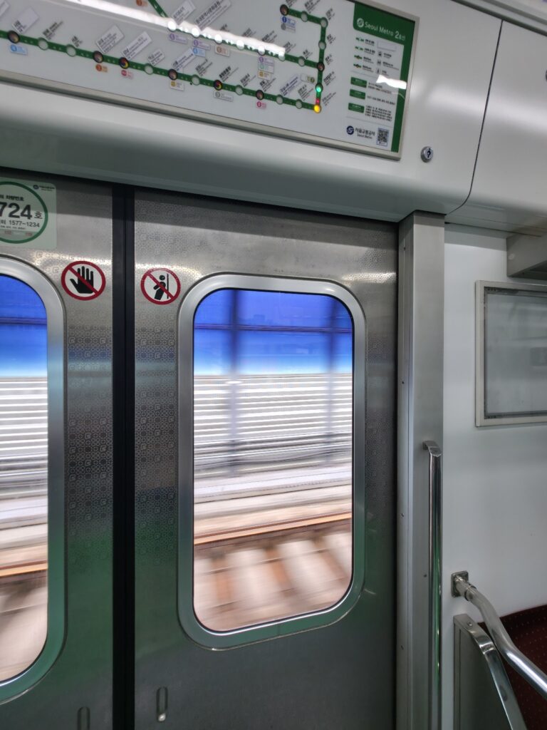 View from inside a Seoul subway car through the window, showing the urban skyline along the route.