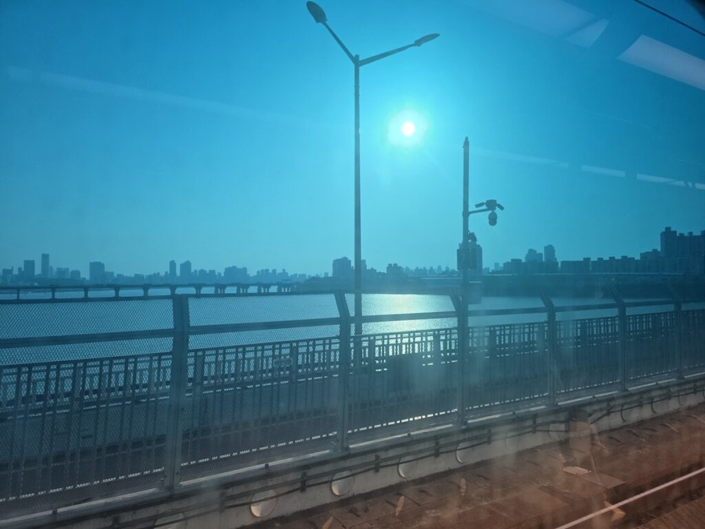 A scenic view of the Han River and Seoul skyline through a blue-tinted subway window during Seoul summer travel.