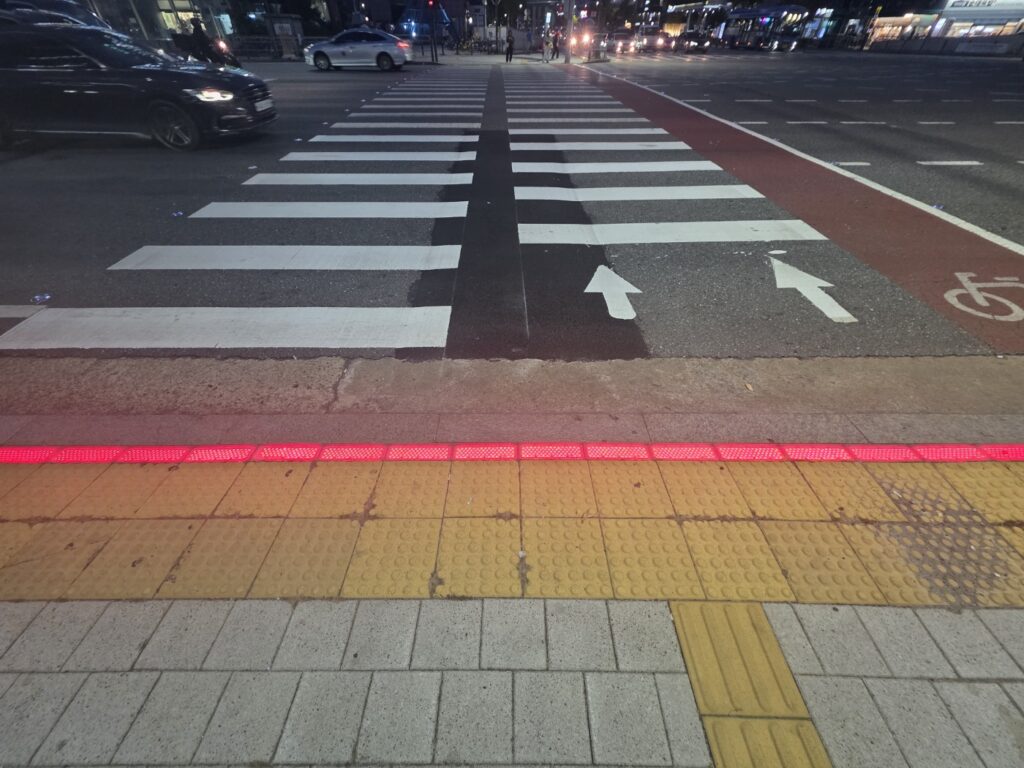 A close-up view of a crosswalk edge with LED red floor lights and tactile paving for the visually impaired.