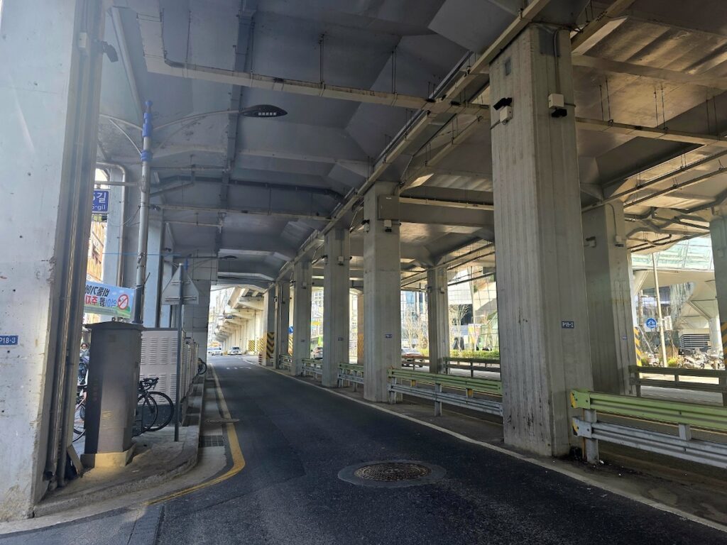 A long perspective of massive concrete bridge pillars over a quiet road, symbolizing the urban scale and subterranean pulse in the Seoul Transportation Guide 2026.