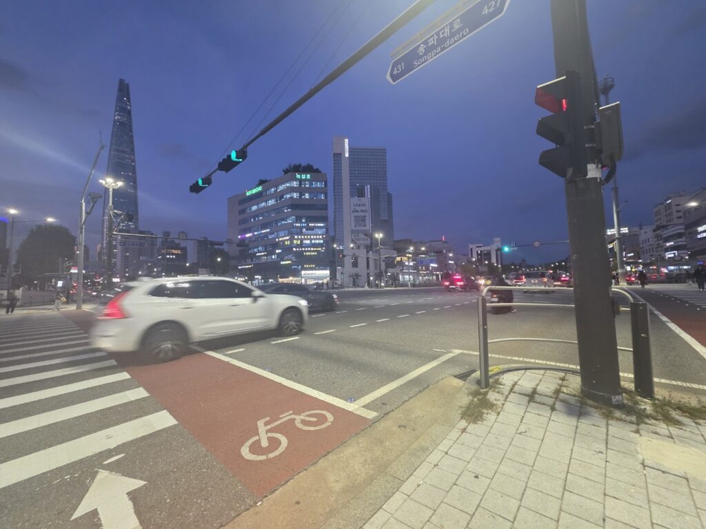 Cars crossing a wide intersection on Songpa-daero in Seoul with green pedestrian lights glowing.