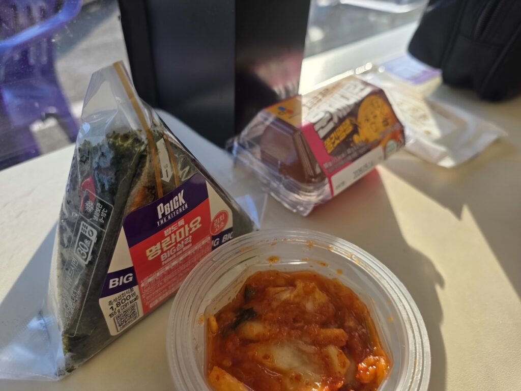 south-korea-convenience-stores-kimbap-eggs-kimchi A spread of triangle kimbap, roasted eggs, and a small container of kimchi on a table at a Korean convenience store.