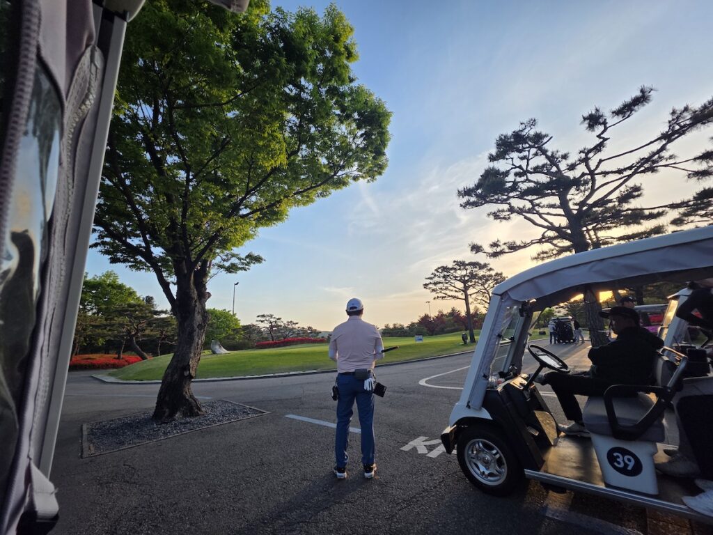 south-korea-golf-prices-daytime-tee-off A golfer in a pink shirt standing near a golf cart during a daytime round at a lush Korean golf course.