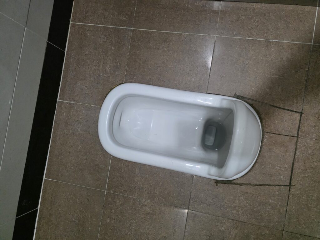 "A close-up view of a Korean squat toilet highlighting its porcelain surface and flush system, representing traditional yet hygienic restroom design in Korea."
