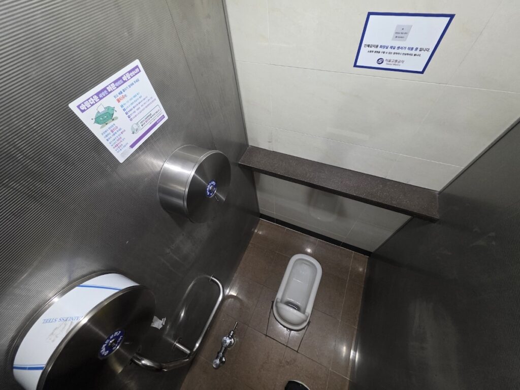 "A full view of a traditional squat toilet inside a Korean public restroom, showing the clean design and tiled floor commonly found in subway stations."