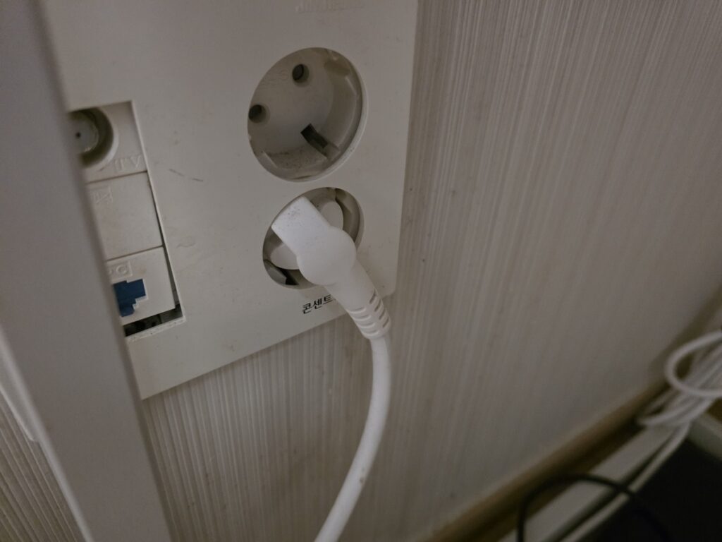A close-up of a white South Korean 220V electrical outlet (Type F) featured in the Korea Travel Adapter Guide.