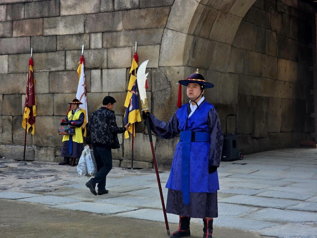 A close-up of a royal guardian in a blue and purple traditional uniform holding a long bladed weapon at Sungnyemun Gate during the Pasu Ritual.