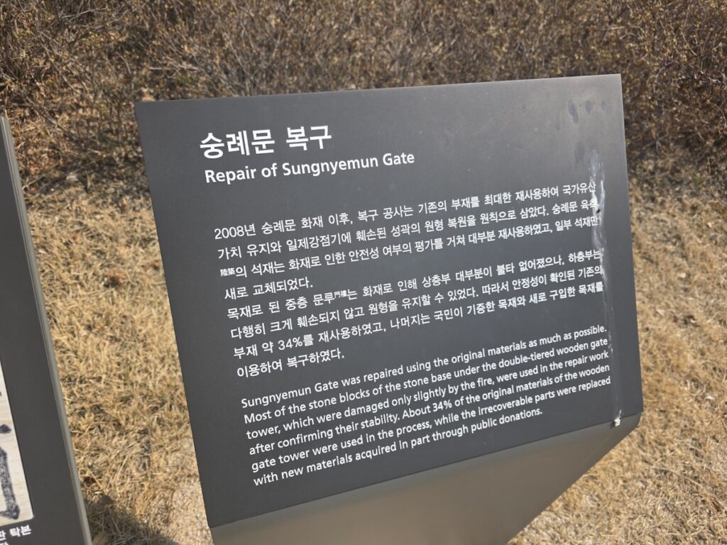 sungnyemun-gate-pasu-ritual-front-view-with-tourists A photo of an information sign detailing the repair and restoration history of Sungnyemun Gate after the tragic 2008 fire.