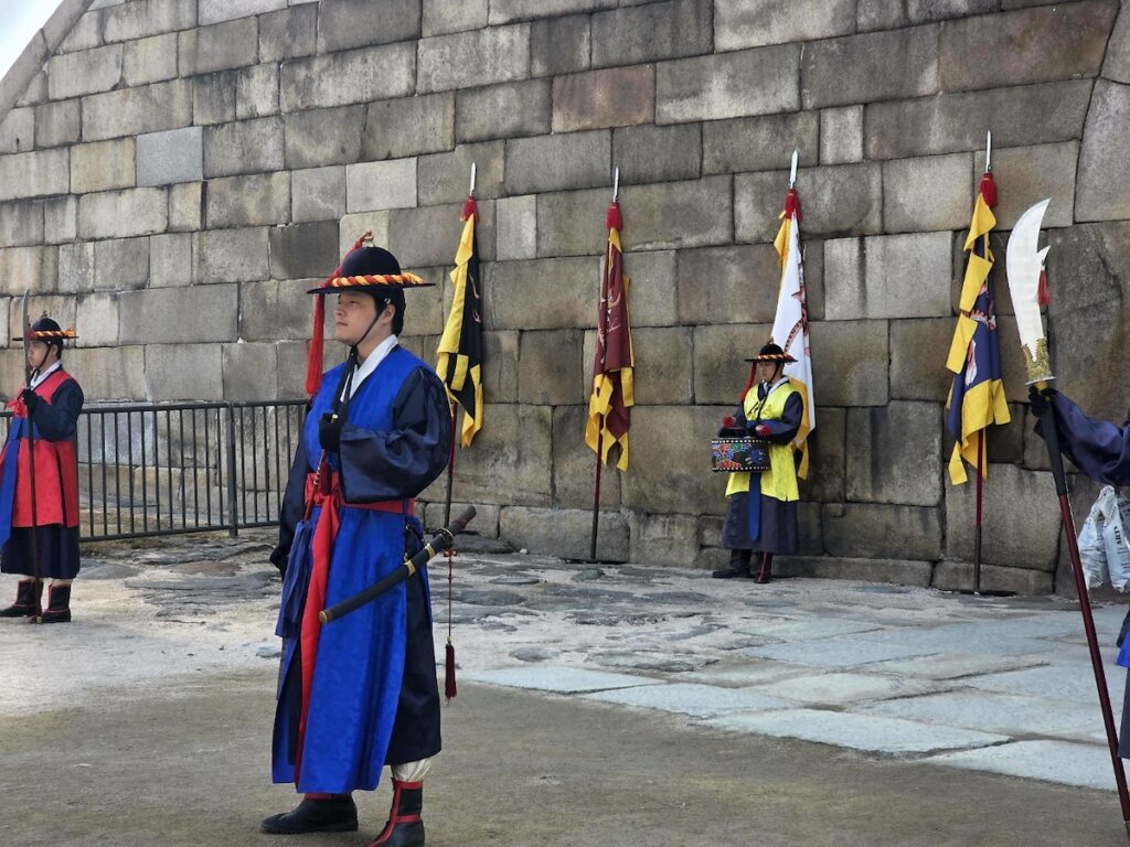 sungnyemun-gate-pasu-ritual-guardians-lineup-side-view A side view of royal guardians in colorful traditional attire standing at attention along the stone fortress wall during the Pasu Ritual.