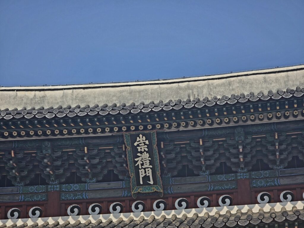 sungnyemun-gate-pasu-ritual-repair-history-sign-info A detailed close-up of the vertical hanging board of Sungnyemun Gate, showing the traditional Chinese characters written by Prince Yangnyeong.