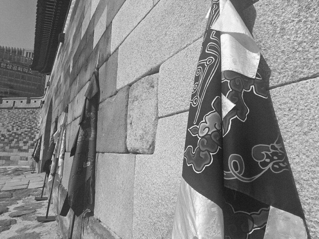 sungnyemun-gate-pasu-ritual-traditional-flags-detail A close-up detail of traditional black and red ritual flags leaning against the ancient stone wall of Sungnyemun Gate.