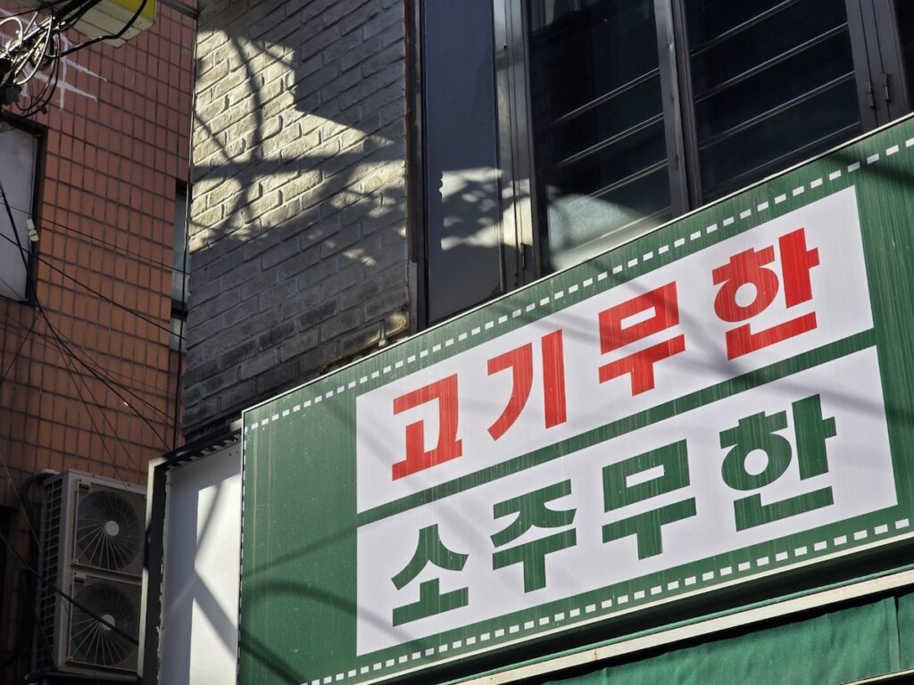 A large green sign offering unlimited meat and soju, a prime example of the "MU" system for those who travel Korea on a budget.