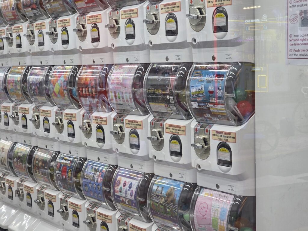 unmanned-gacha-shop-interior-organization A wide view of an organized, unmanned Gacha shop with rows of colorful machines.