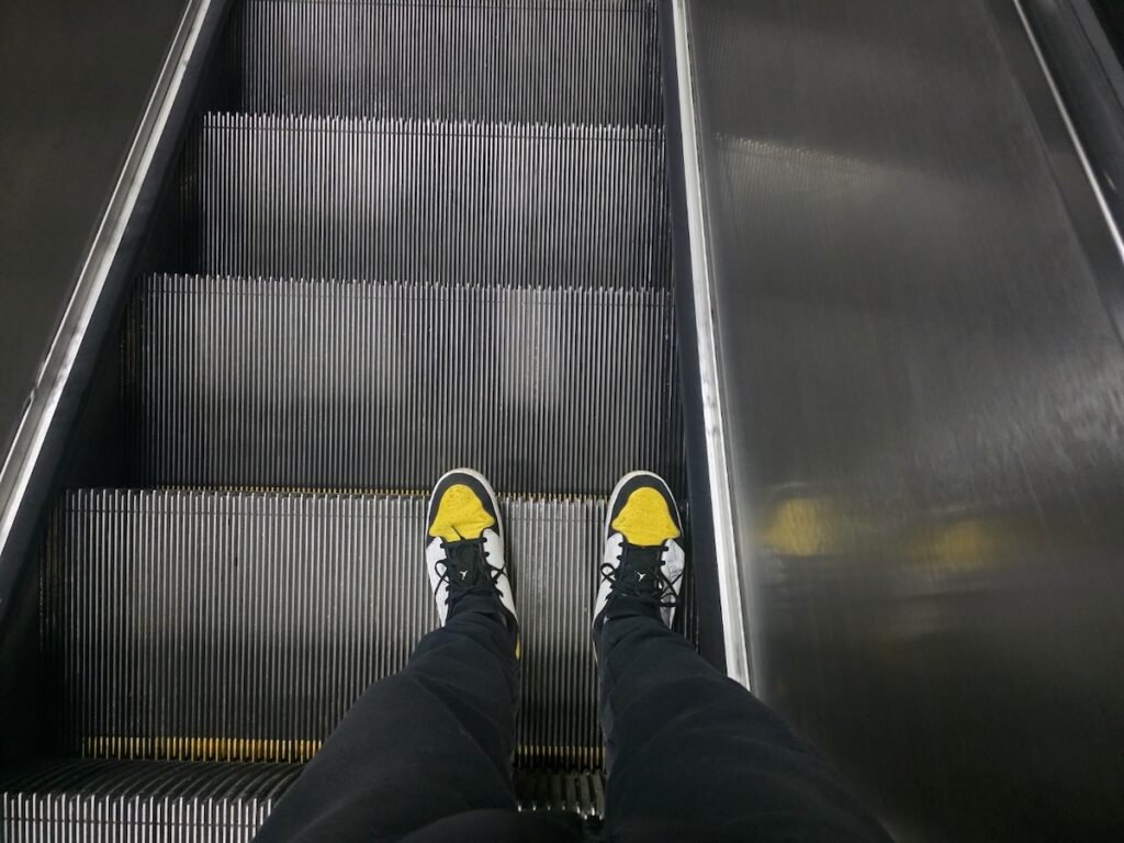 A POV shot wearing yellow sneakers looking down a steep **Korea Subway Escalator**, debating the silent etiquette of Seoul.
