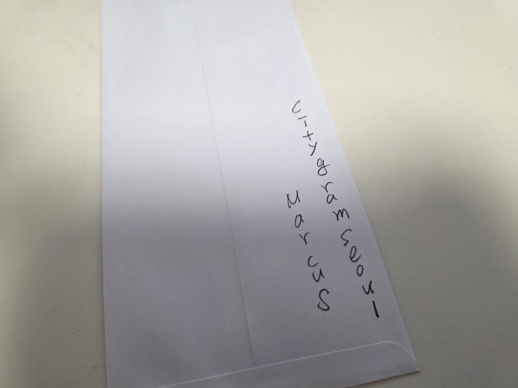 A demonstration of writing a name and affiliation on the back of an envelope for **Korean Funeral Etiquette for Foreigners**.