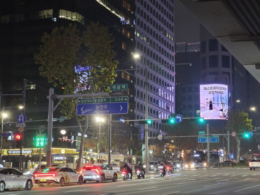 The main road outside Yeoksam Station in Gangnam, with office buildings and pedestrian sidewalks.