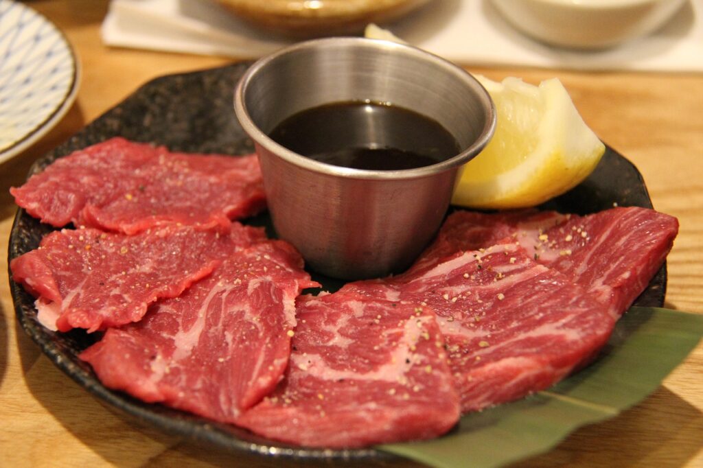Thin slices of raw Hanwoo beef served with sesame oil and salt, known as Korean yuk sashimi, displayed on a chilled plate.